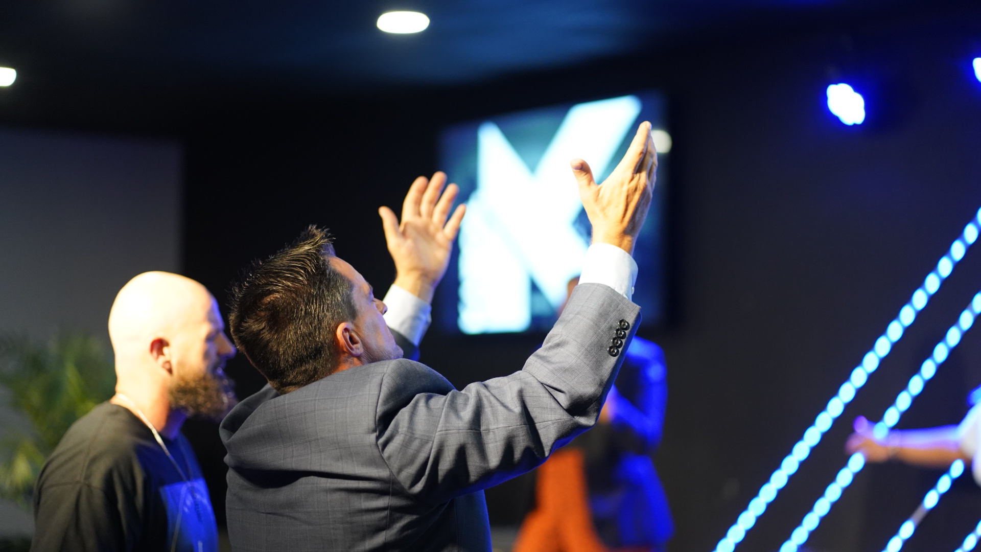 Man in a suit worshipping with hands raised during a Kairos Church service